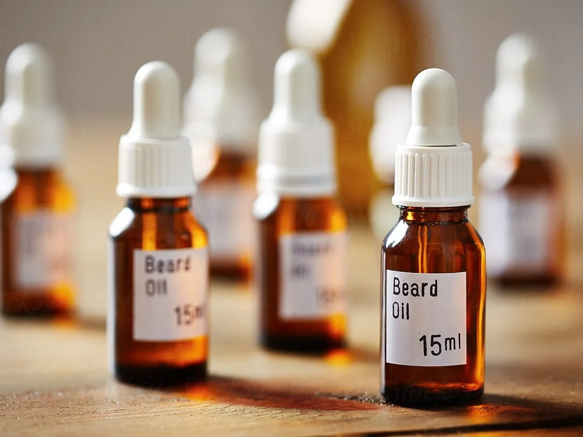 Several small glass bottles labeled 'Beard Oil 15ml' with dropper caps, placed on a wooden table.